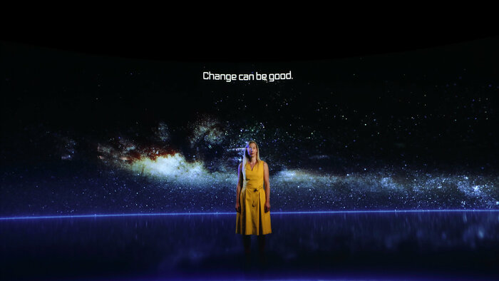 Videostill mit Untertitel "Change can be good", Frau vor einer Aufnahme des Weltalls